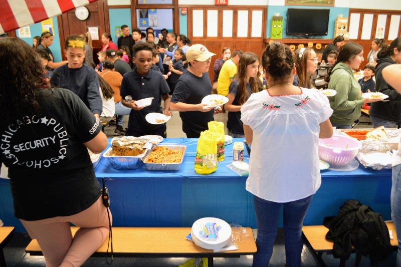 School students standing around a table filled with food, socializing and eating