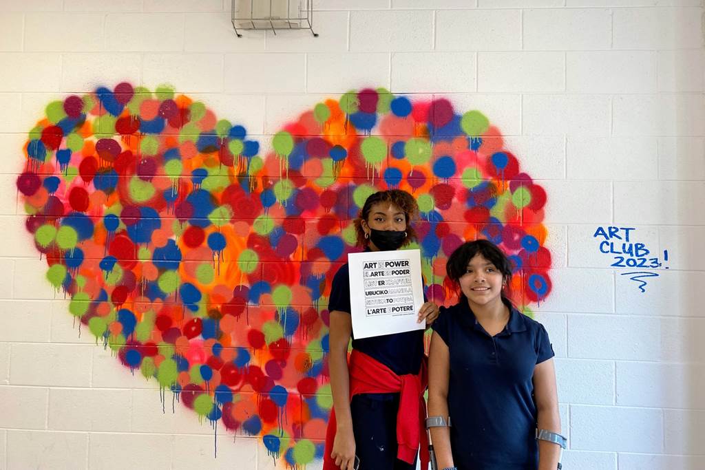 Kaylee and Lucia standing in front of a heart-shaped mural