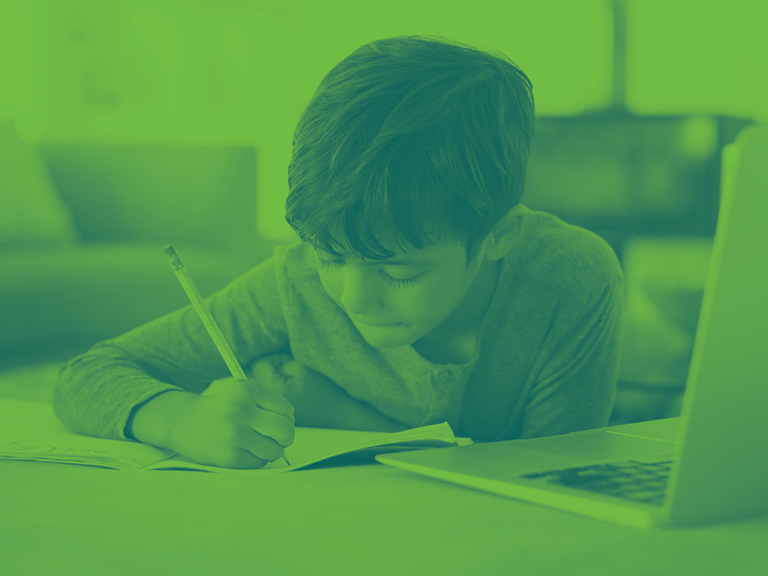 Student taking notes on paper while attending an online class