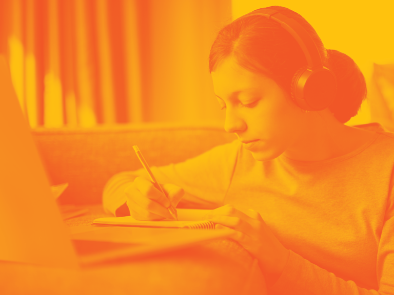 Student taking notes while attending an online class