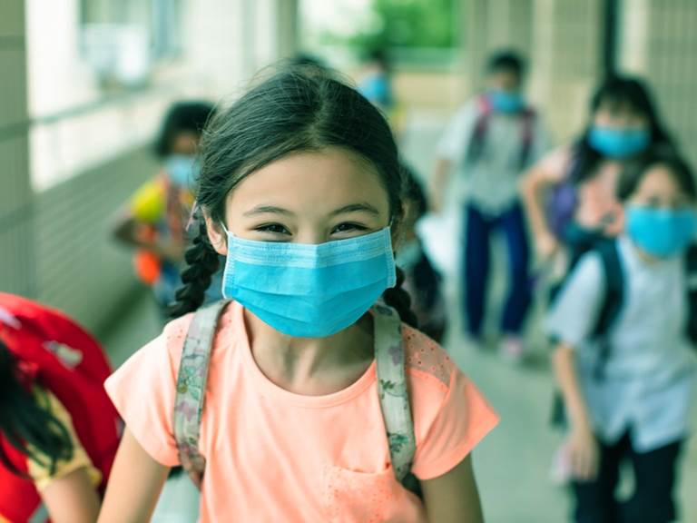 A girl in a mask smiles at school
