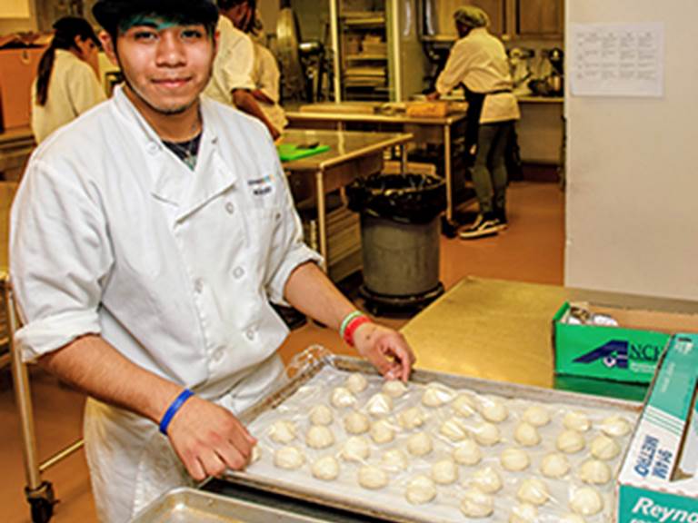 Student smiling while holding a cookie sheet full of dough