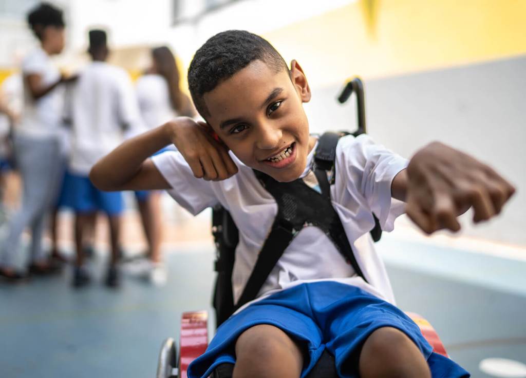 child in a wheelchair waving a hand