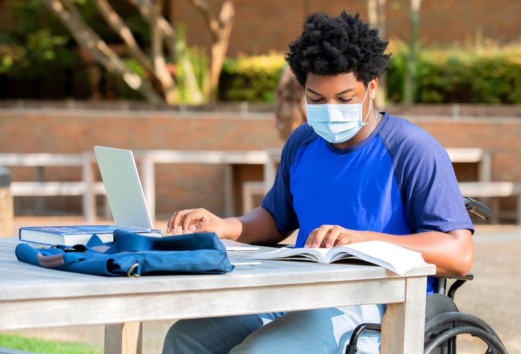 student in wheelchair sitting at table using laptop