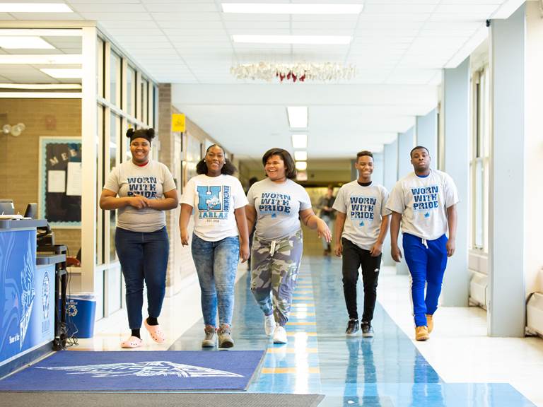 Five high school students walking down a school hallway
