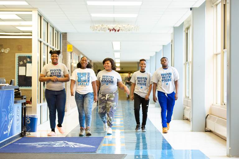 Five high school students walking down a school hallway