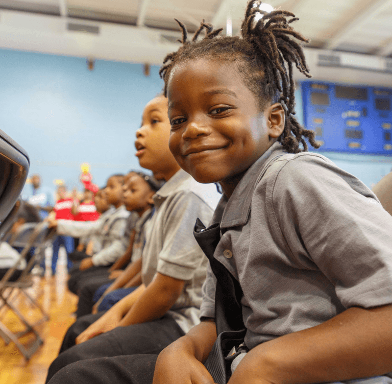 child sitting with other children in gym smiling
