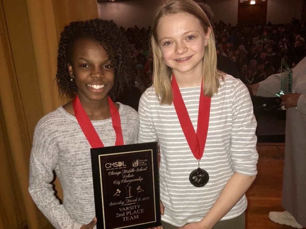 Two smiling girls hold a plaque