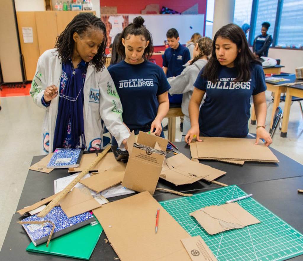 A teacher stand with students with cardboard