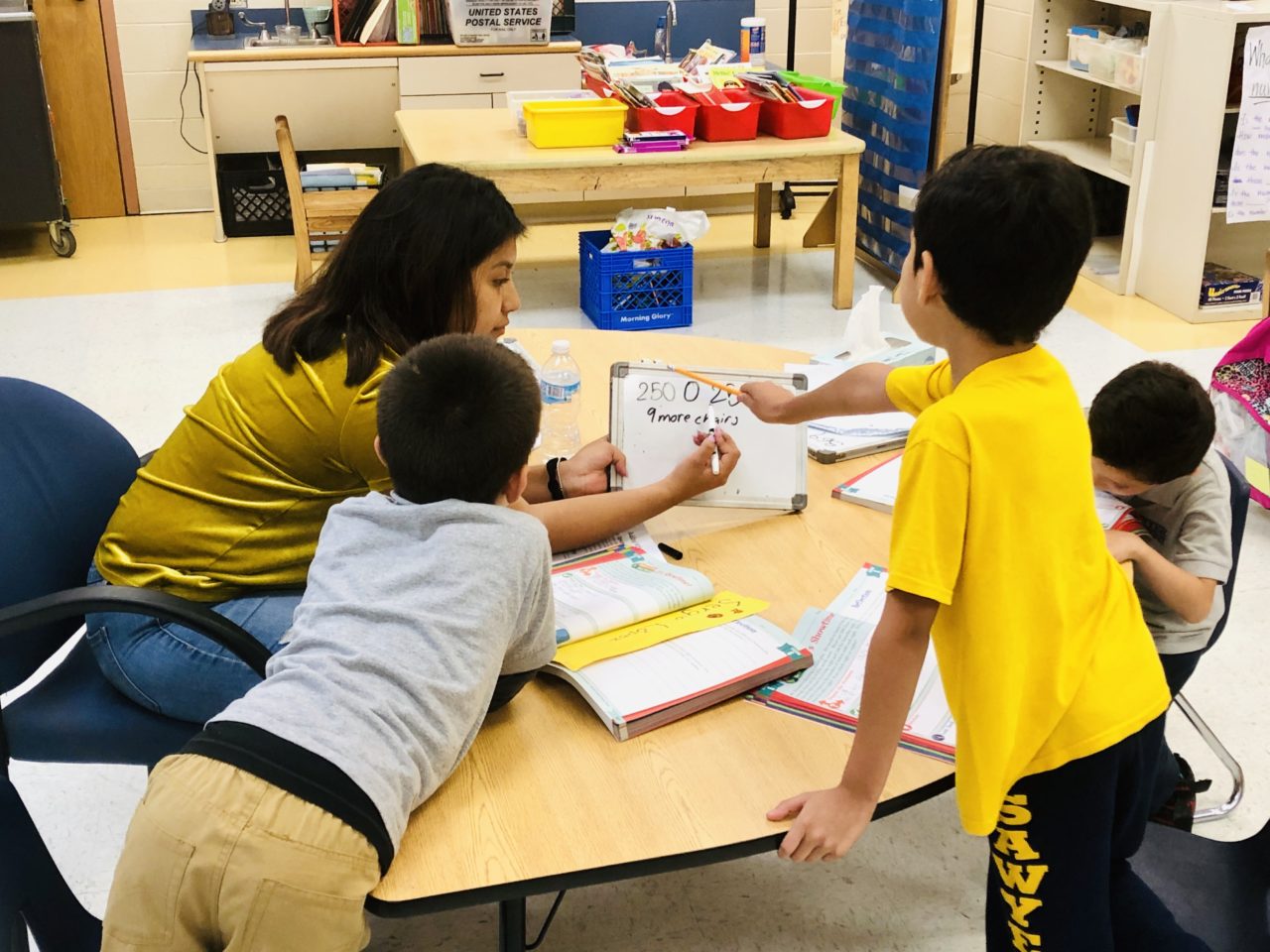 Students surround teacher as she draws on a white board