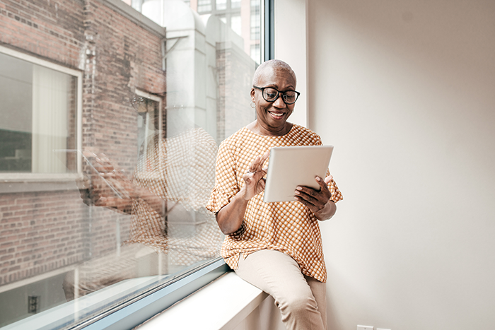 woman leaning on a window reading a tablet